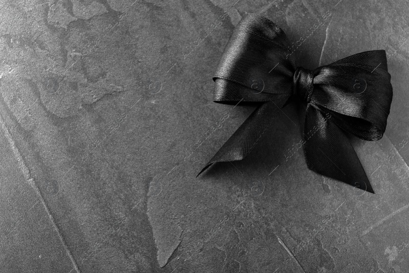 Photo of Black ribbon bow on dark grey stone surface, top view with space for text. Funeral symbol