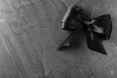 Photo of Black ribbon bow on dark grey stone surface, top view with space for text. Funeral symbol