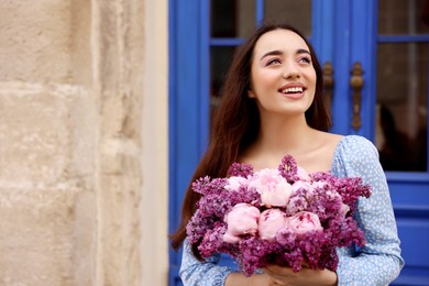 Photo of Beautiful woman with bouquet of spring flowers near building outdoors, space for text