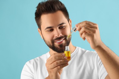 Handsome man with cosmetic serum in hands on light blue background