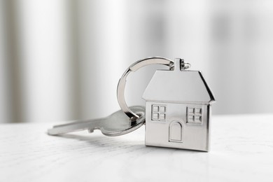 Key with keychain in shape of house on white wooden table indoors, closeup