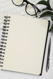 Open notebook, keyboard, pen and glasses on white table, flat lay