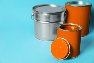 Photo of Cans and bucket of orange paint on turquoise background. Space for text