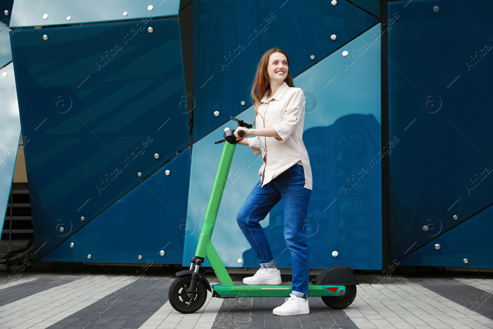 Photo of Happy woman with modern electric kick scooter on city street