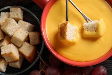 Pot of tasty cheese fondue and forks with bread pieces on table, flat lay