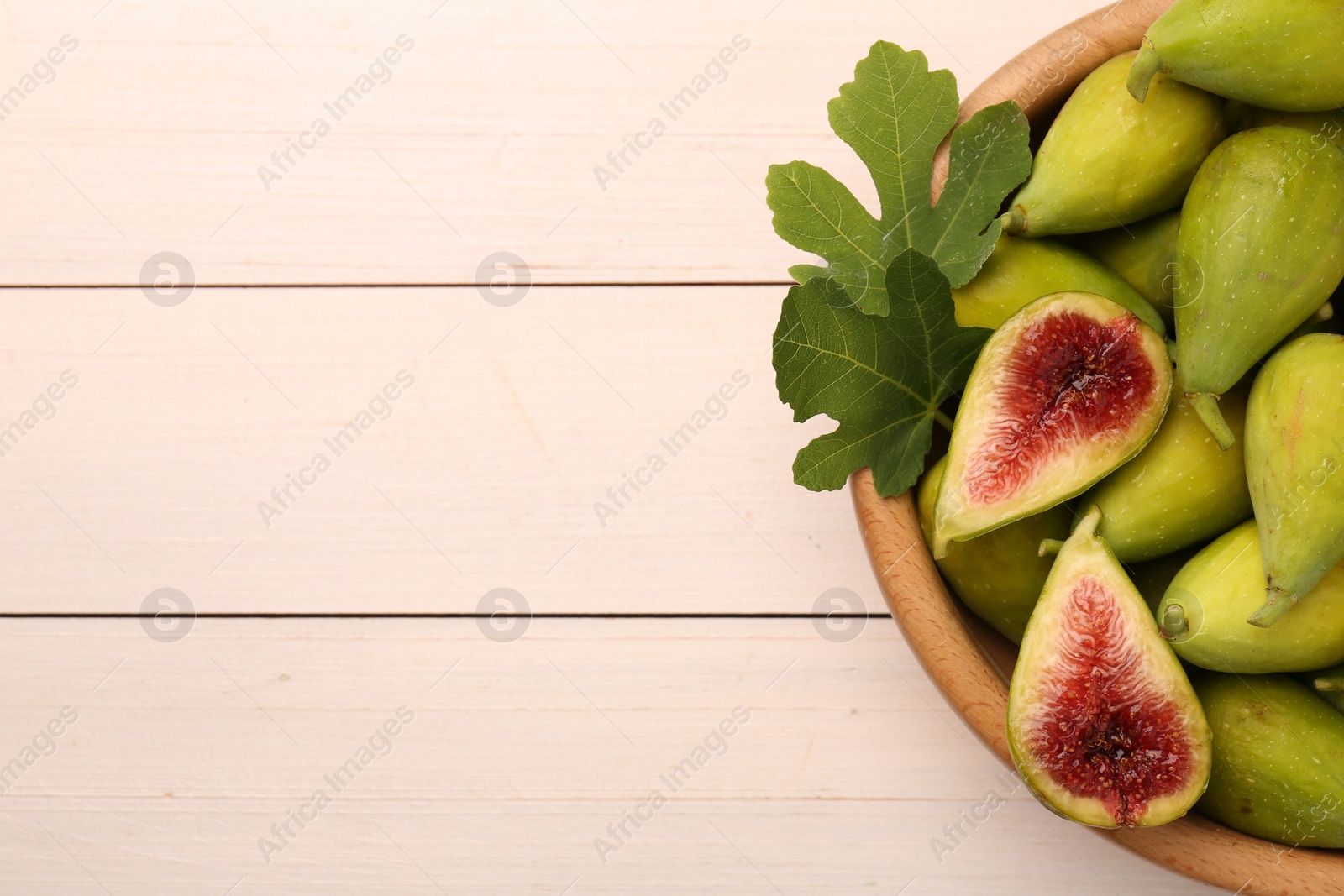 Photo of Cut and whole fresh green figs on white wooden table, top view. Space for text