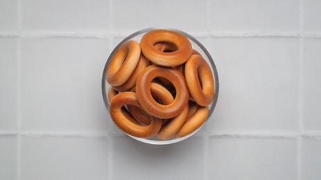 Photo of Bowl of tasty dry bagels (sushki) on white tiled table, top view