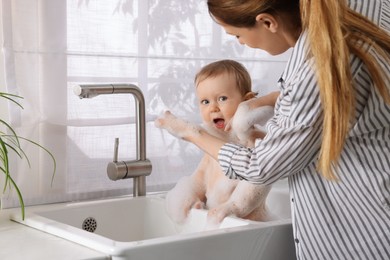 Mother washing her little baby in sink at home