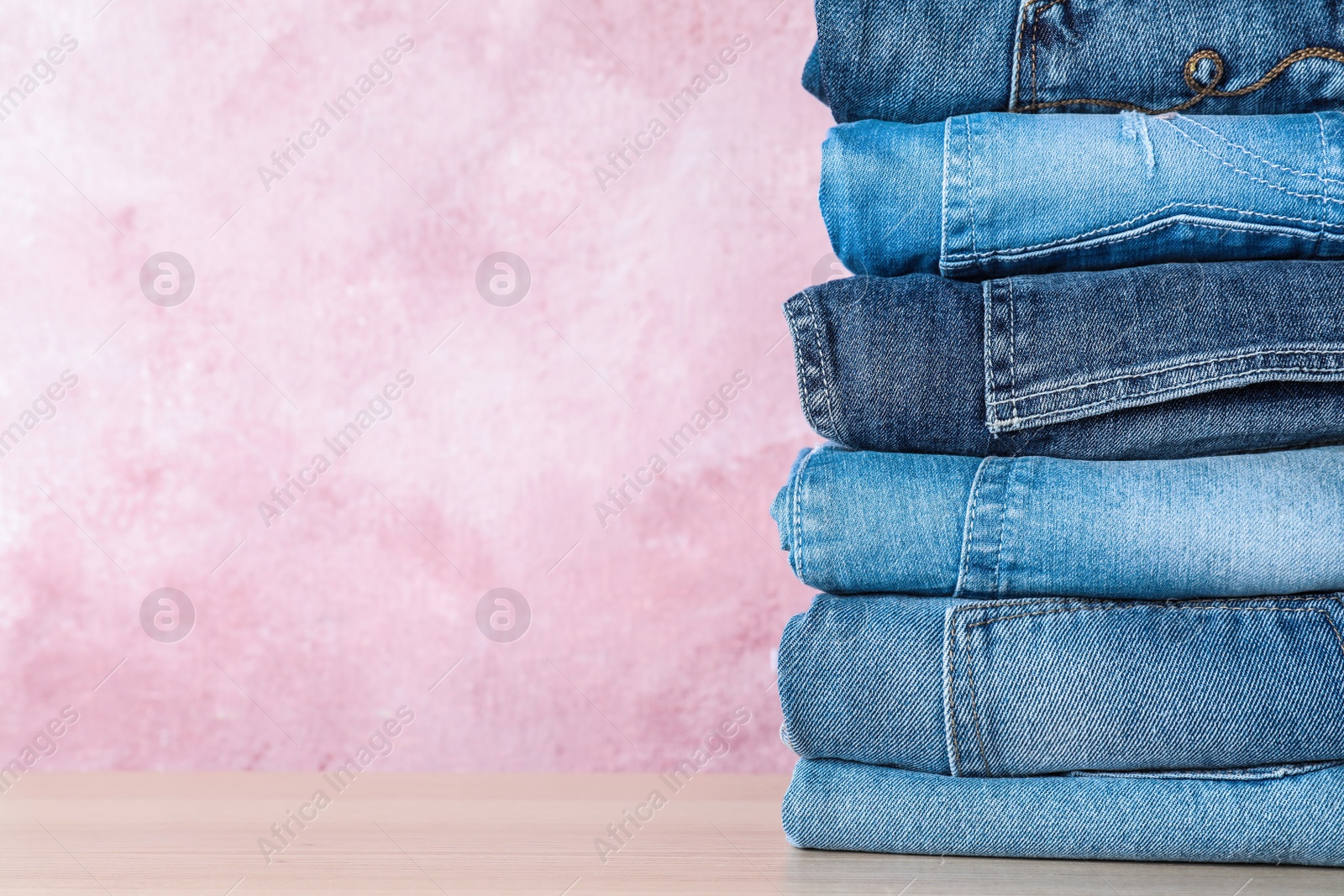 Photo of Stack of different jeans on wooden table against pink background. Space for text