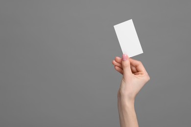 Woman holding blank business card on grey background, closeup. Space for text