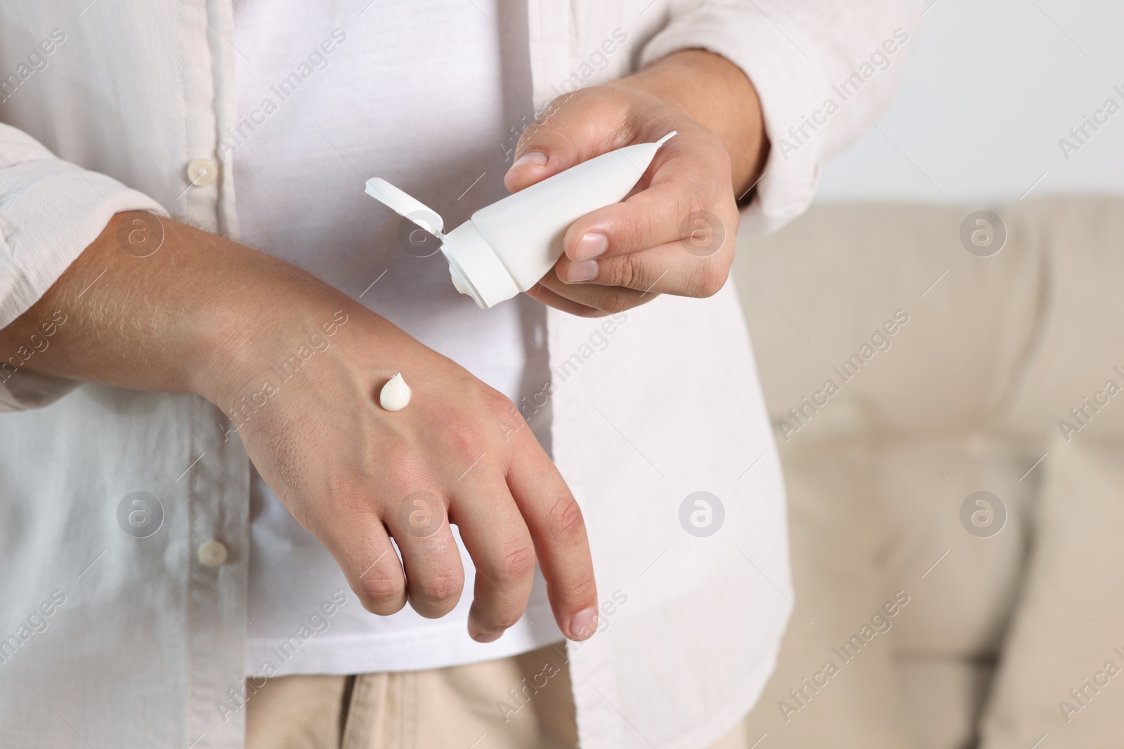 Photo of Man applying hand cream from tube at home, closeup