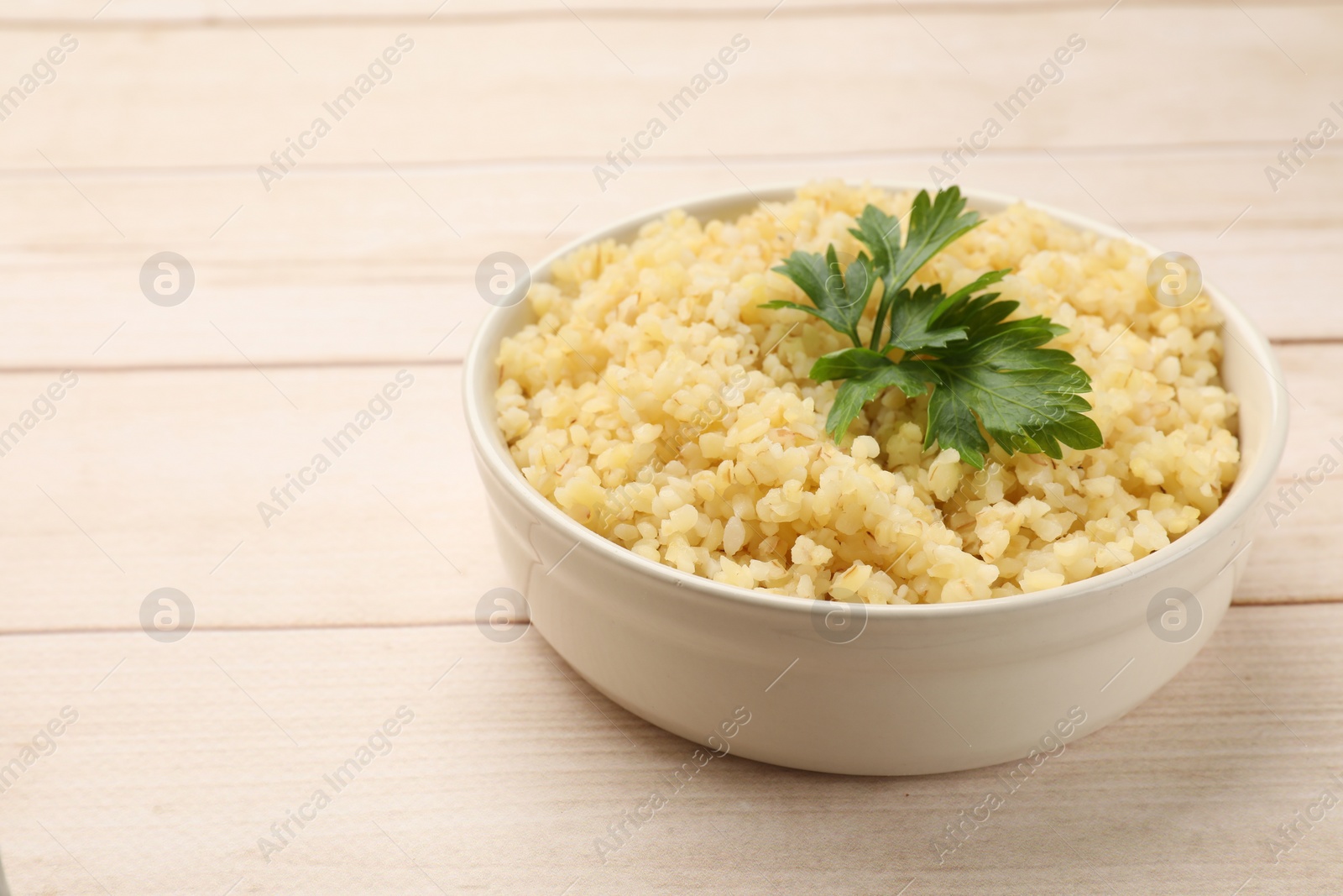 Photo of Delicious bulgur with parsley in bowl on wooden table, closeup. Space for text