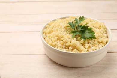 Photo of Delicious bulgur with parsley in bowl on wooden table, closeup. Space for text