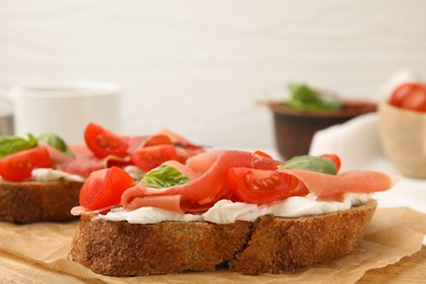 Photo of Tasty bruschettas with prosciutto, tomatoes and cheese on wooden board, closeup