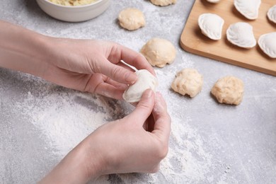 Photo of Woman making dumplings (varenyky) at grey table, closeup