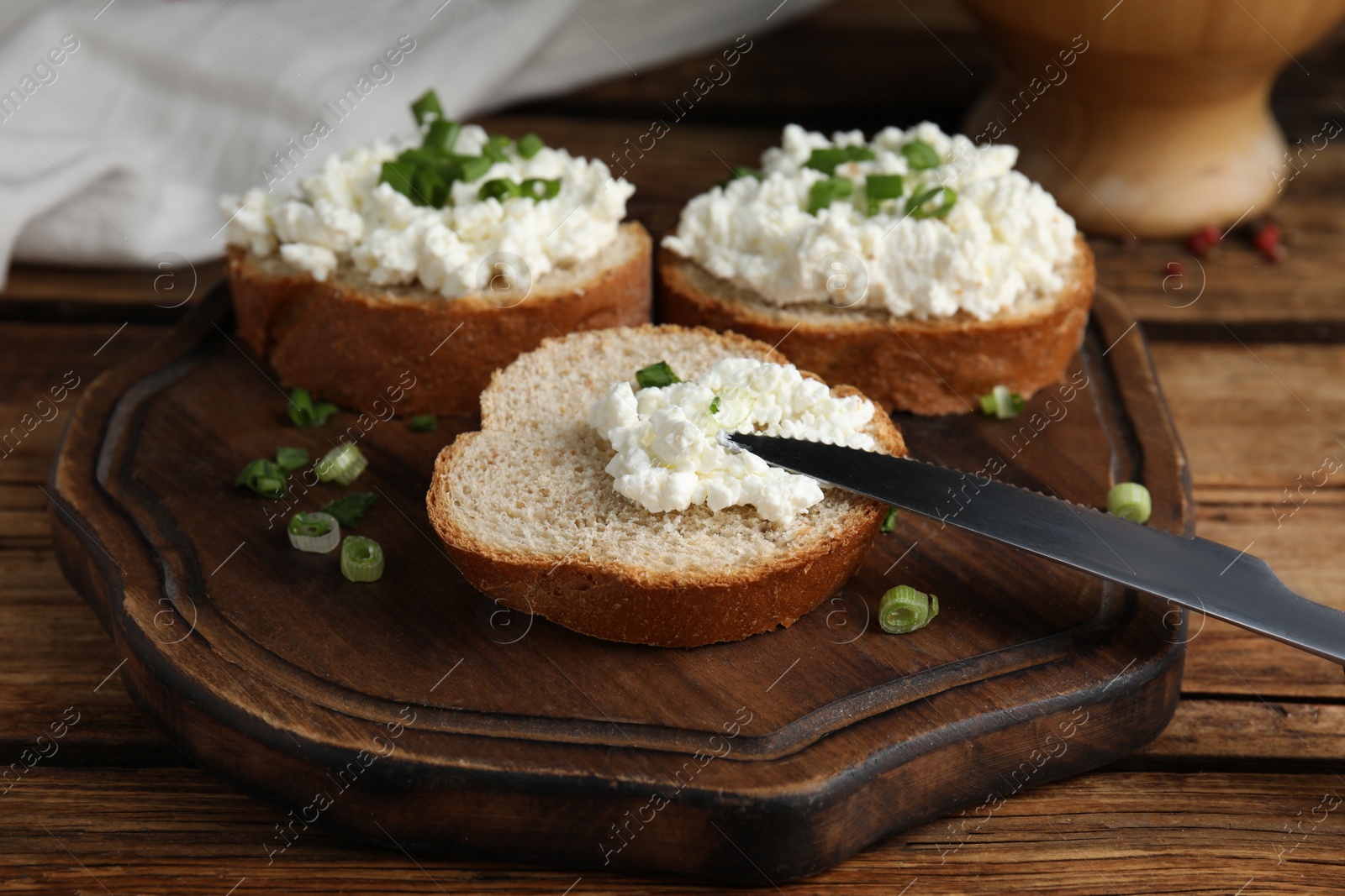 Photo of Bread with cottage cheese and green onion on wooden table, closeup