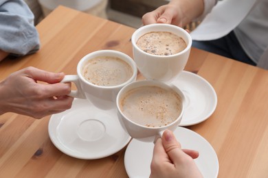 Photo of Women clinking cups of coffee at table in cafe, closeup