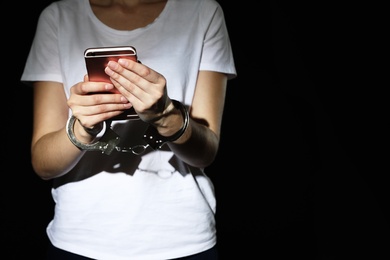 Woman in handcuffs using smartphone on black background, closeup with space for text. Solitude concept