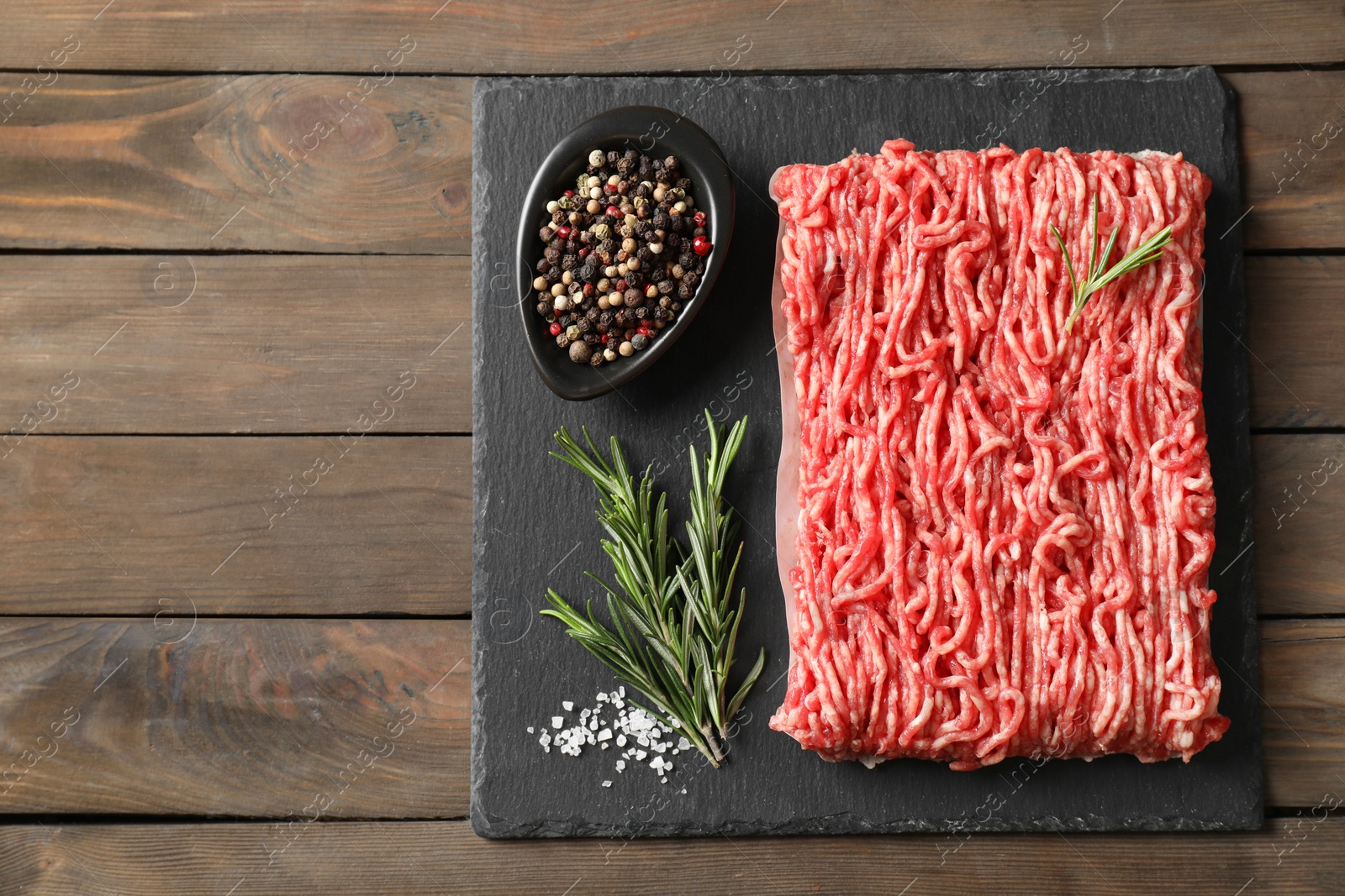 Photo of Raw ground meat, spices and rosemary on wooden table, top view. Space for text