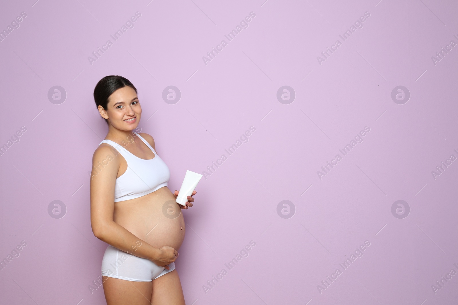 Photo of Pregnant woman holding body cream on color background with space for text