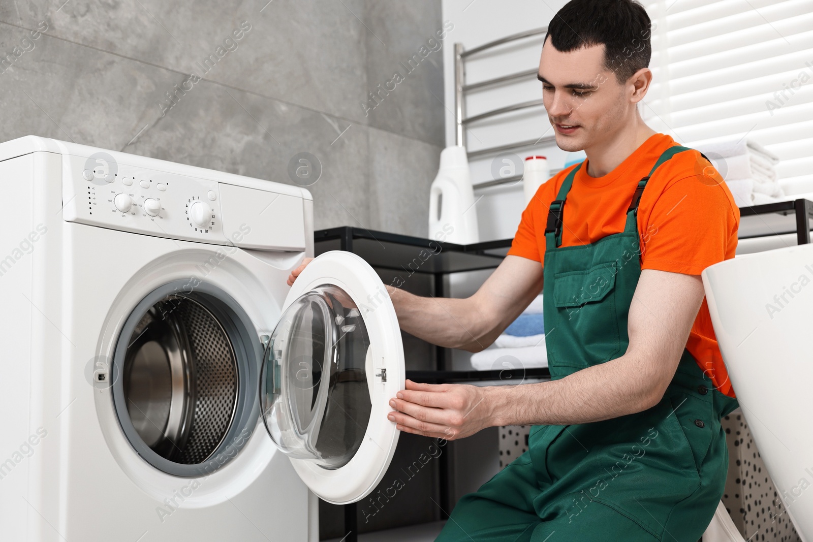 Photo of Young plumber repairing washing machine in bathroom, low angle view