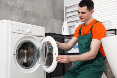 Young plumber repairing washing machine in bathroom, low angle view