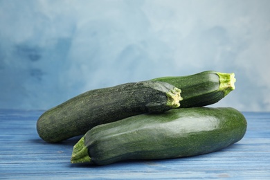 Photo of Fresh ripe green zucchinis on wooden table against blue background, space for text