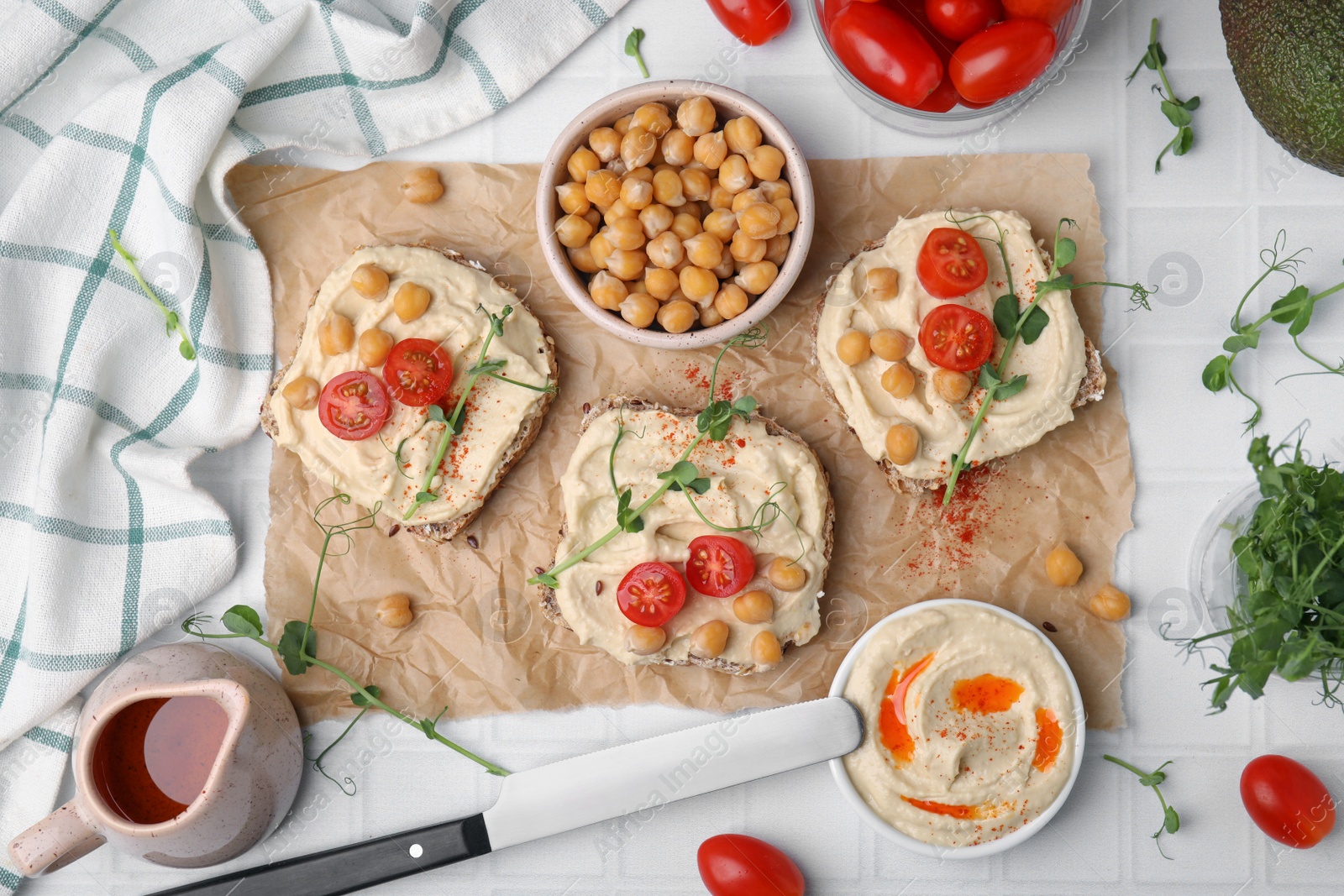 Photo of Delicious sandwiches with hummus and ingredients on white tiled table, flat lay