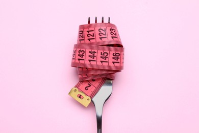 Photo of Fork with measuring tape on pink background, top view. Diet concept