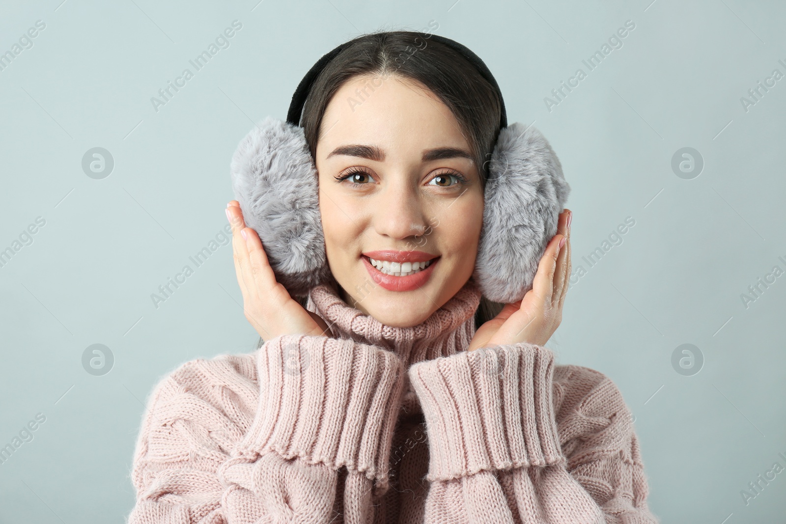 Photo of Beautiful young woman wearing earmuffs on light grey background