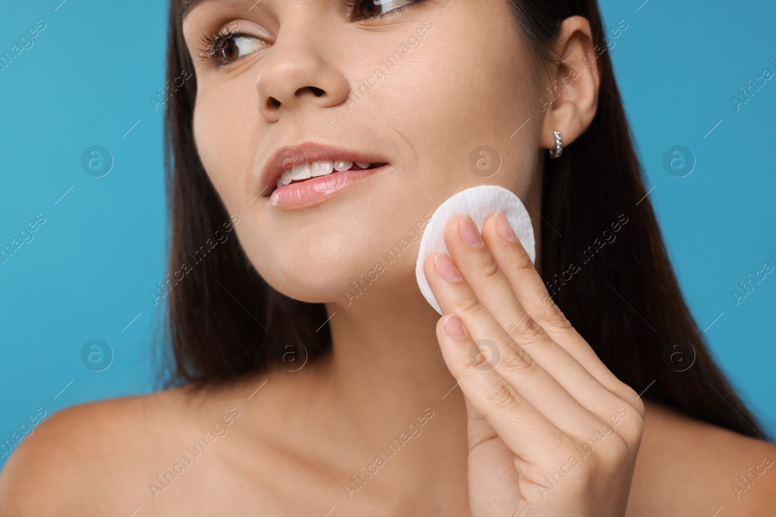 Photo of Young woman with cotton pad on light blue background, closeup