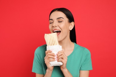 Photo of Young woman eating delicious shawarma on red background