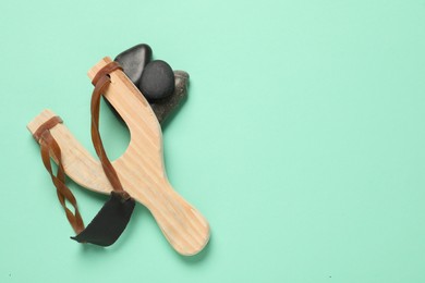 Wooden slingshot with stones on light green background, top view. Space for text