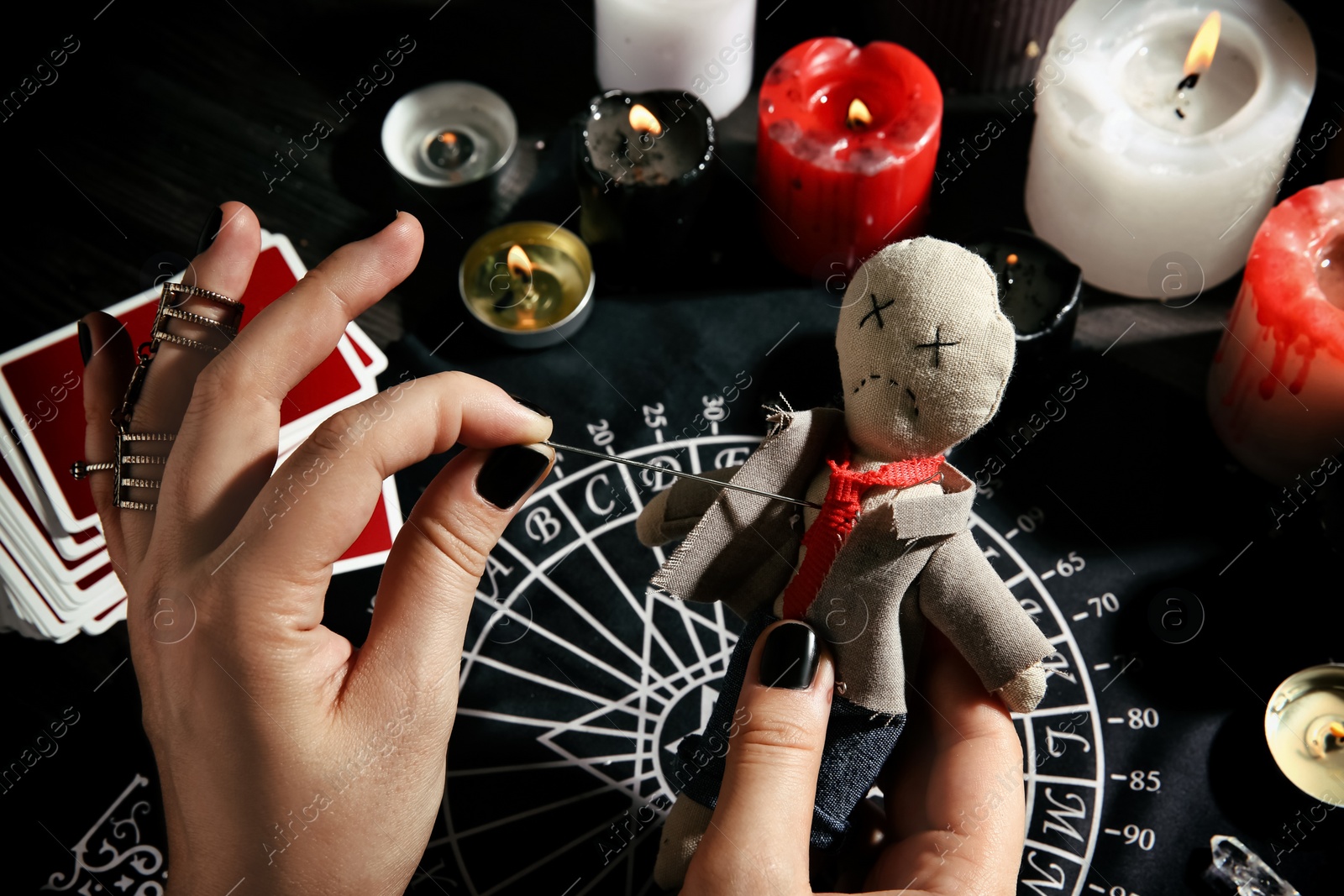 Photo of Woman stabbing voodoo doll with needle at table, closeup. Curse ceremony