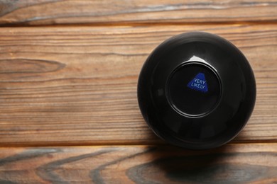 Photo of Magic eight ball with prediction Very Likely on wooden table, space for text