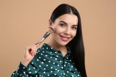 Photo of Beautiful woman applying makeup on light brown background