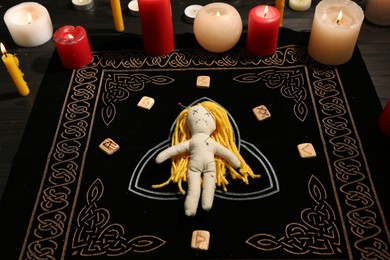 Photo of Voodoo doll pierced with pins, runes and candles on black mat. Curse ceremony