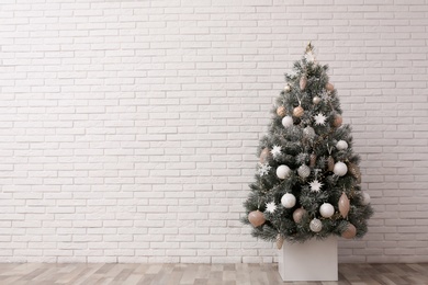 Photo of Beautifully decorated Christmas tree near white brick wall, space for text
