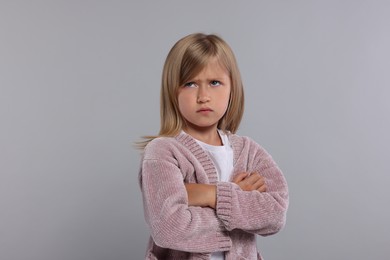 Resentful girl with crossed arms on grey background