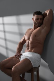 Photo of Young man in stylish white underwear sitting on chair near grey wall