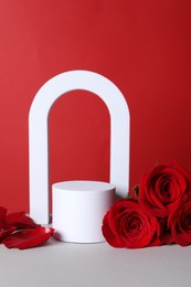 Photo of Stylish presentation for product. Beautiful roses, petals and geometric figures on white table against red background