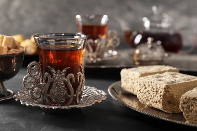 Photo of Turkish tea and sweets served in vintage tea set on black table, closeup