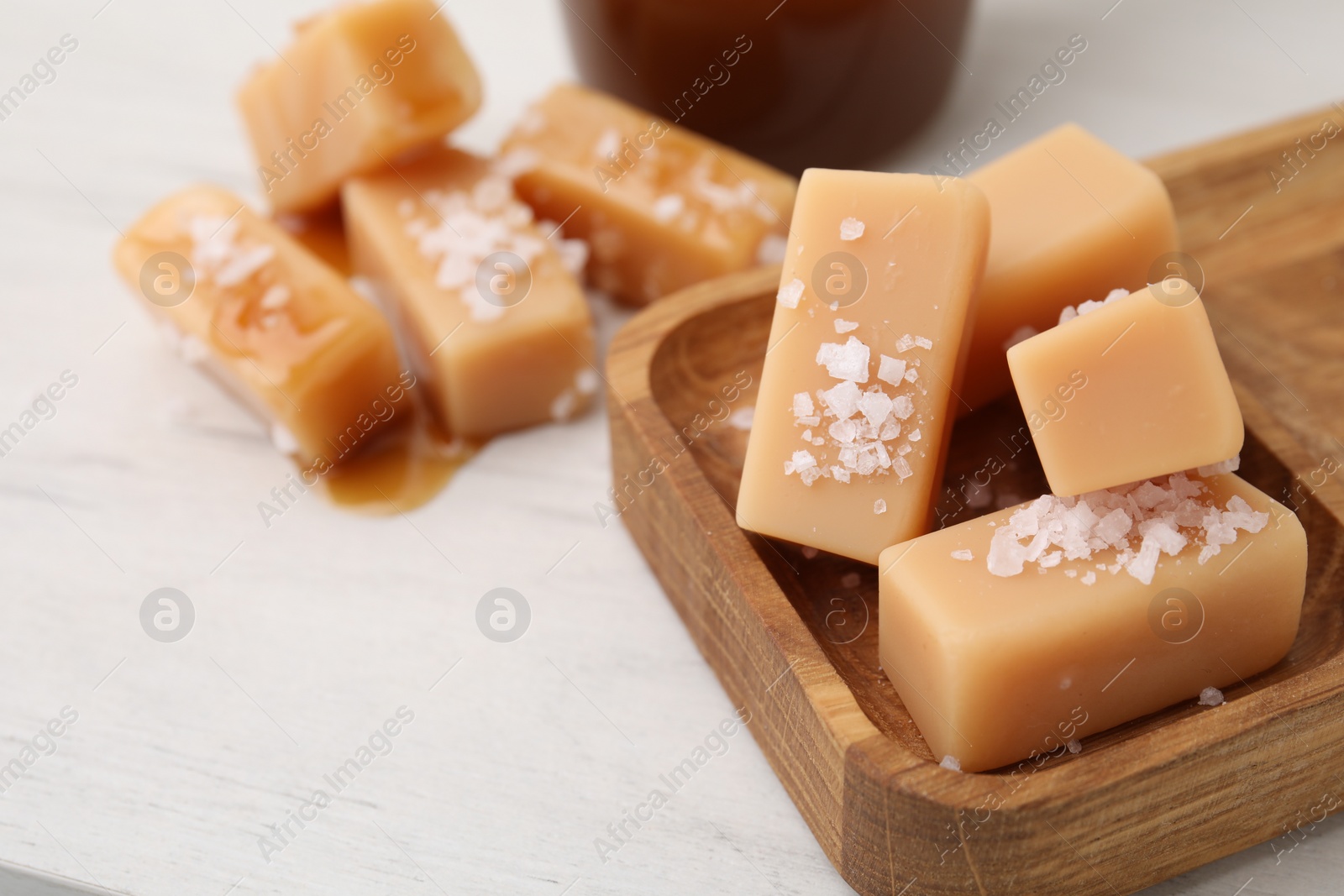 Photo of Yummy caramel candies, sauce and sea salt on white wooden table, closeup