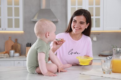 Happy young woman feeding her cute little baby at table in kitchen