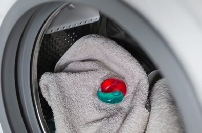 Photo of Laundry detergent capsule and towel in washing machine drum, closeup view