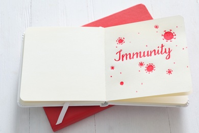 Photo of Notebook with word Immunity on white wooden table