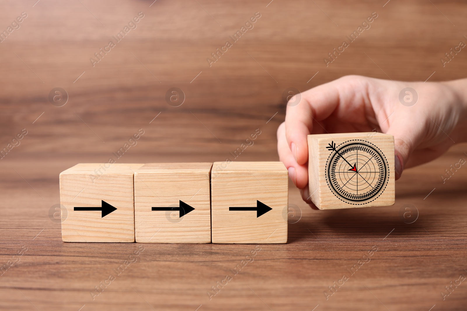 Image of Woman putting cube with icon of target into row of cubes with arrows against on wooden background, closeup