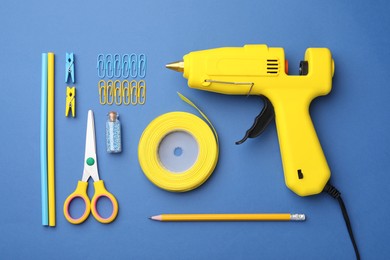 Photo of Hot glue gun and handicraft materials on blue background, flat lay