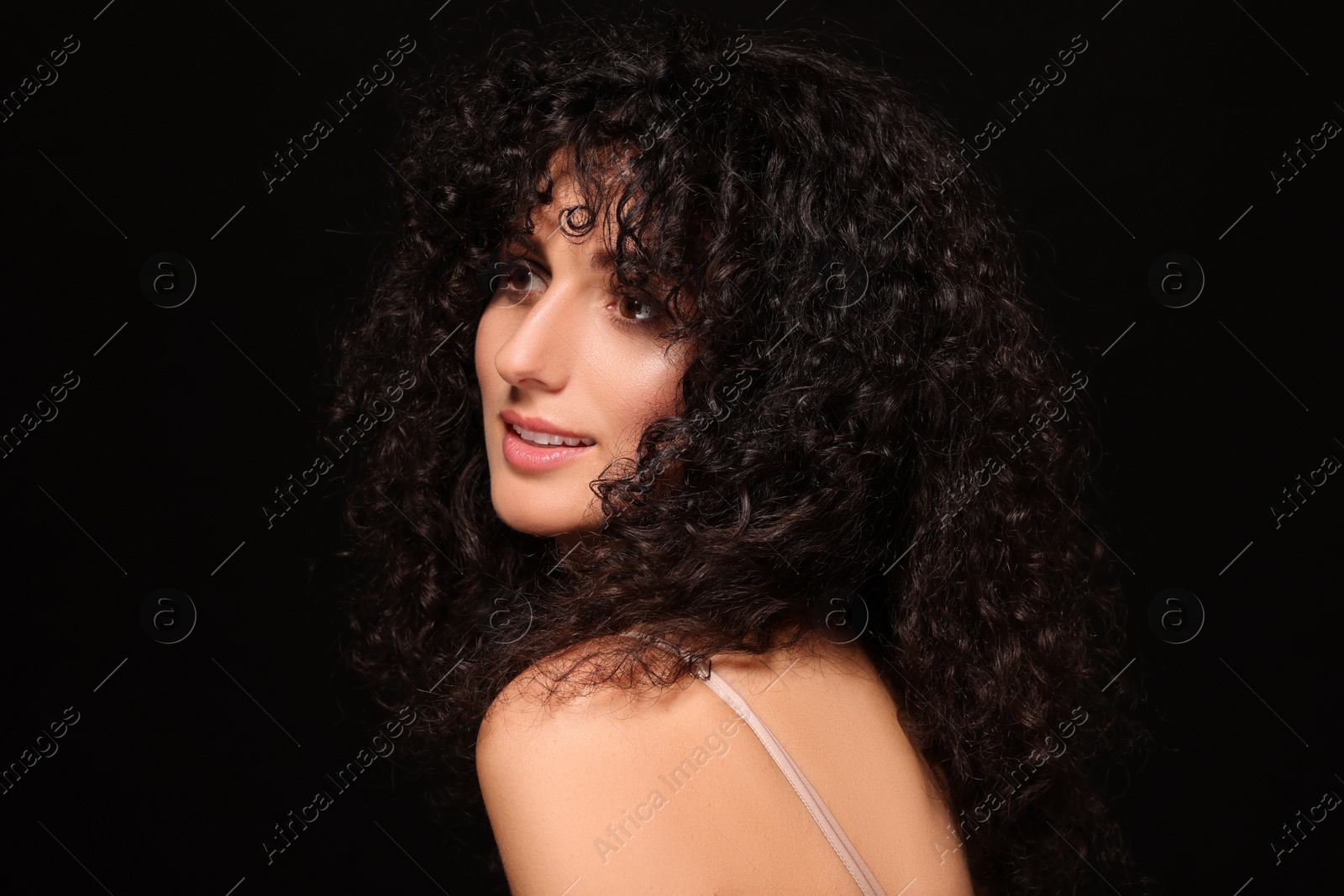 Photo of Beautiful young woman with long curly hair on black background