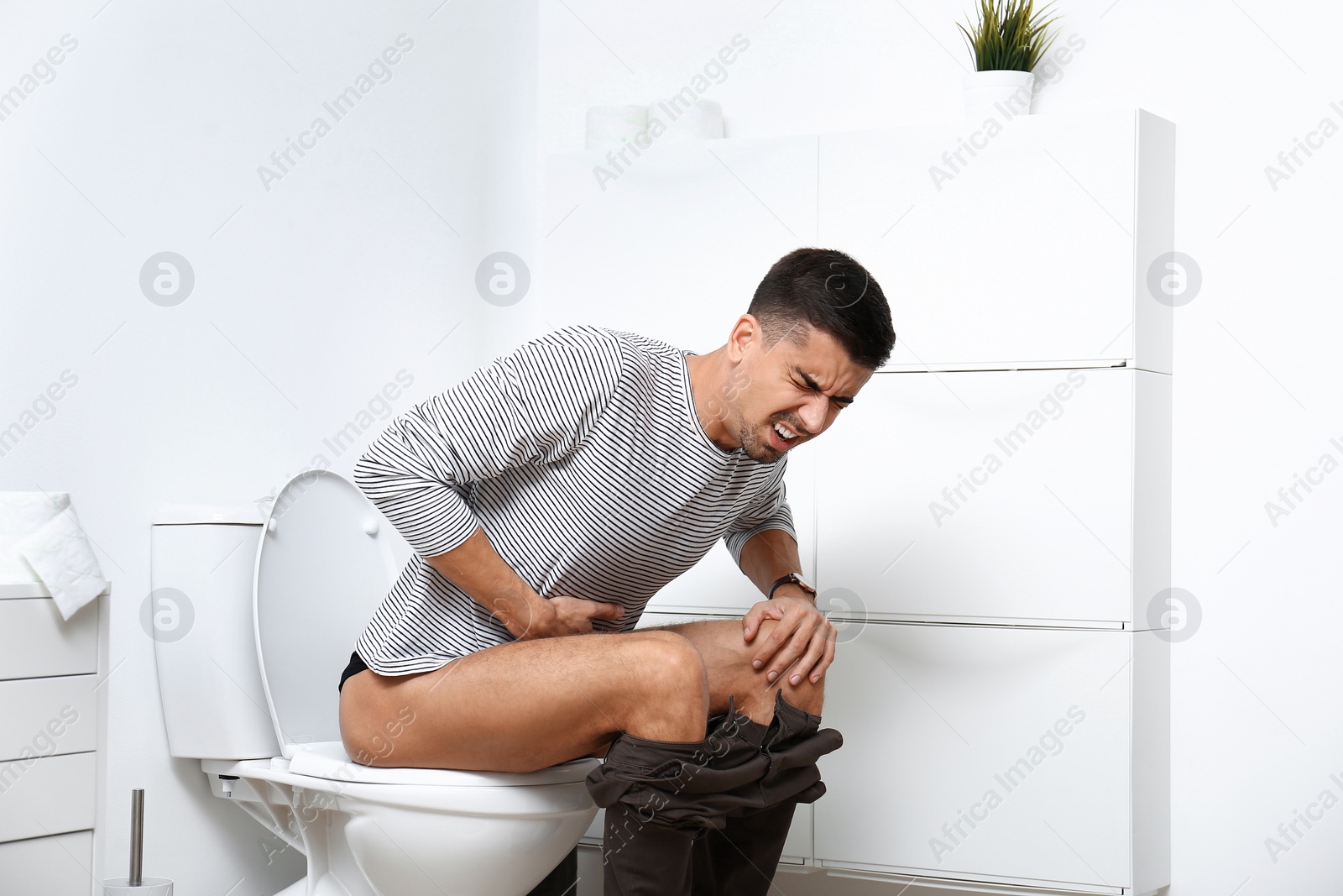 Photo of Man with stomach ache sitting on toilet bowl in bathroom